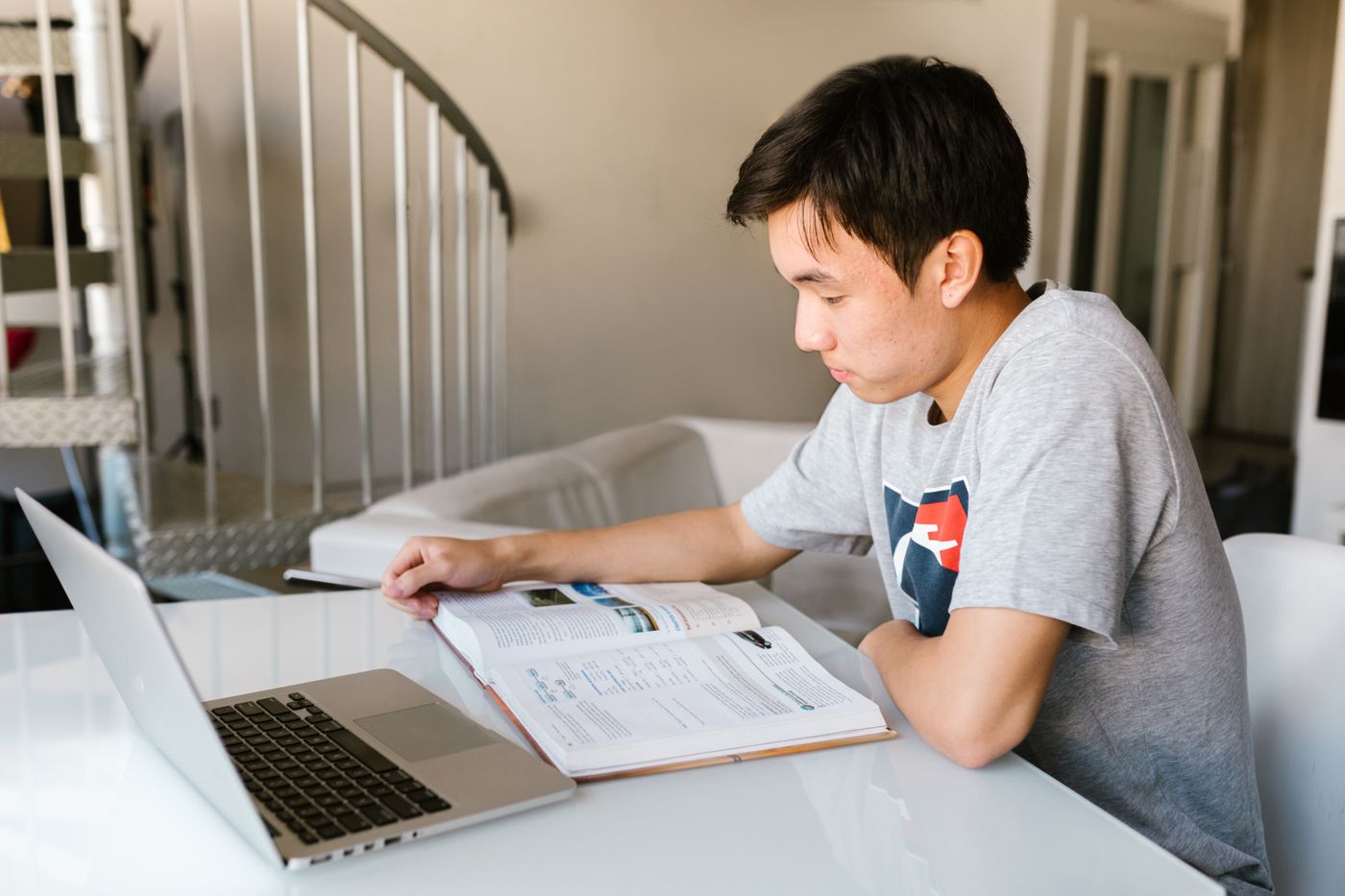 A high school student studying at home with a laptop and textbook